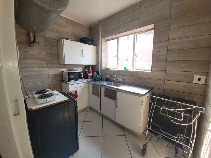 A compact kitchen featuring tiled walls and flooring, stainless steel sink, and built-in cabinetry, offering a functional space ready for modernization.