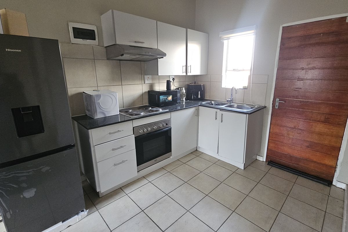 A functional kitchen featuring white cabinetry, a built-in oven and hob, extractor fan, double sink, and tiled flooring with direct exterior access.
