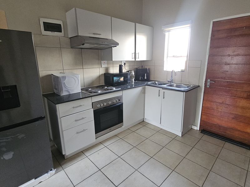 A functional kitchen featuring white cabinetry, a built-in oven and hob, extractor fan, double sink, and tiled flooring with direct exterior access.