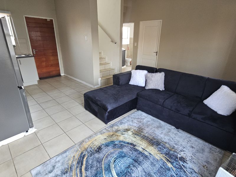 Open plan living area featuring tiled flooring, a staircase, and access to the kitchen and adjacent rooms.