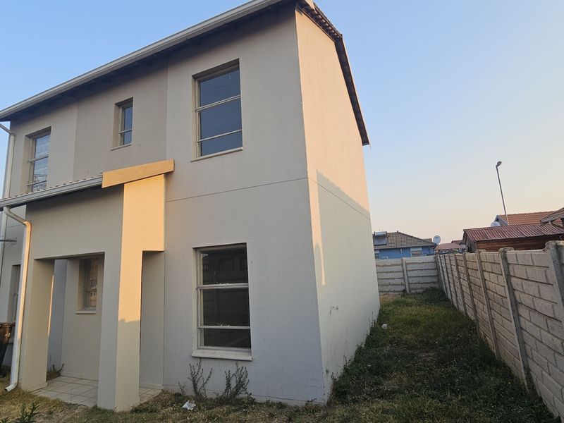 A two-story residential house featuring a neutral facade, aluminium window frames, and a surrounding precast concrete boundary wall.