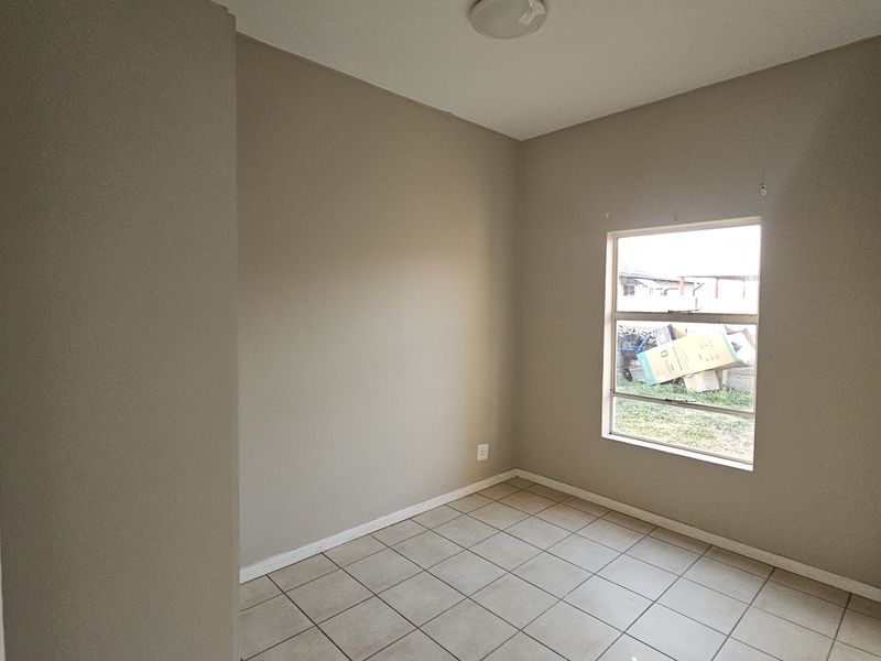 A vacant bedroom featuring neutral wall paint, tiled flooring, and a sliding window providing natural light.