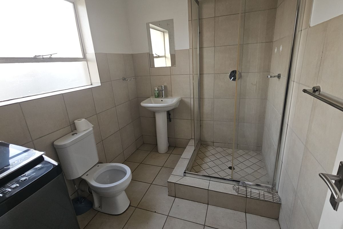 A functional bathroom featuring a pedestal basin, a glass-enclosed shower, and neutral wall and floor tiling.