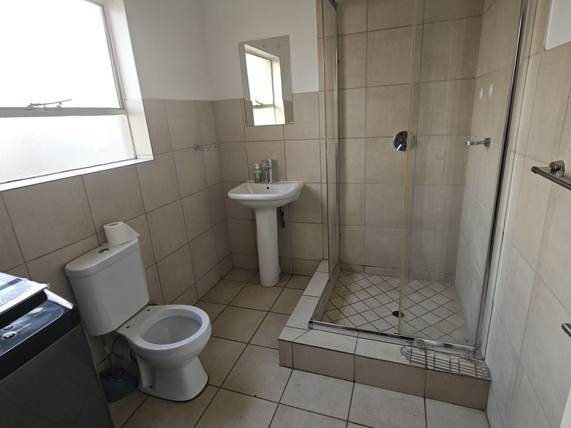 A functional bathroom featuring a pedestal basin, a glass-enclosed shower, and neutral wall and floor tiling.