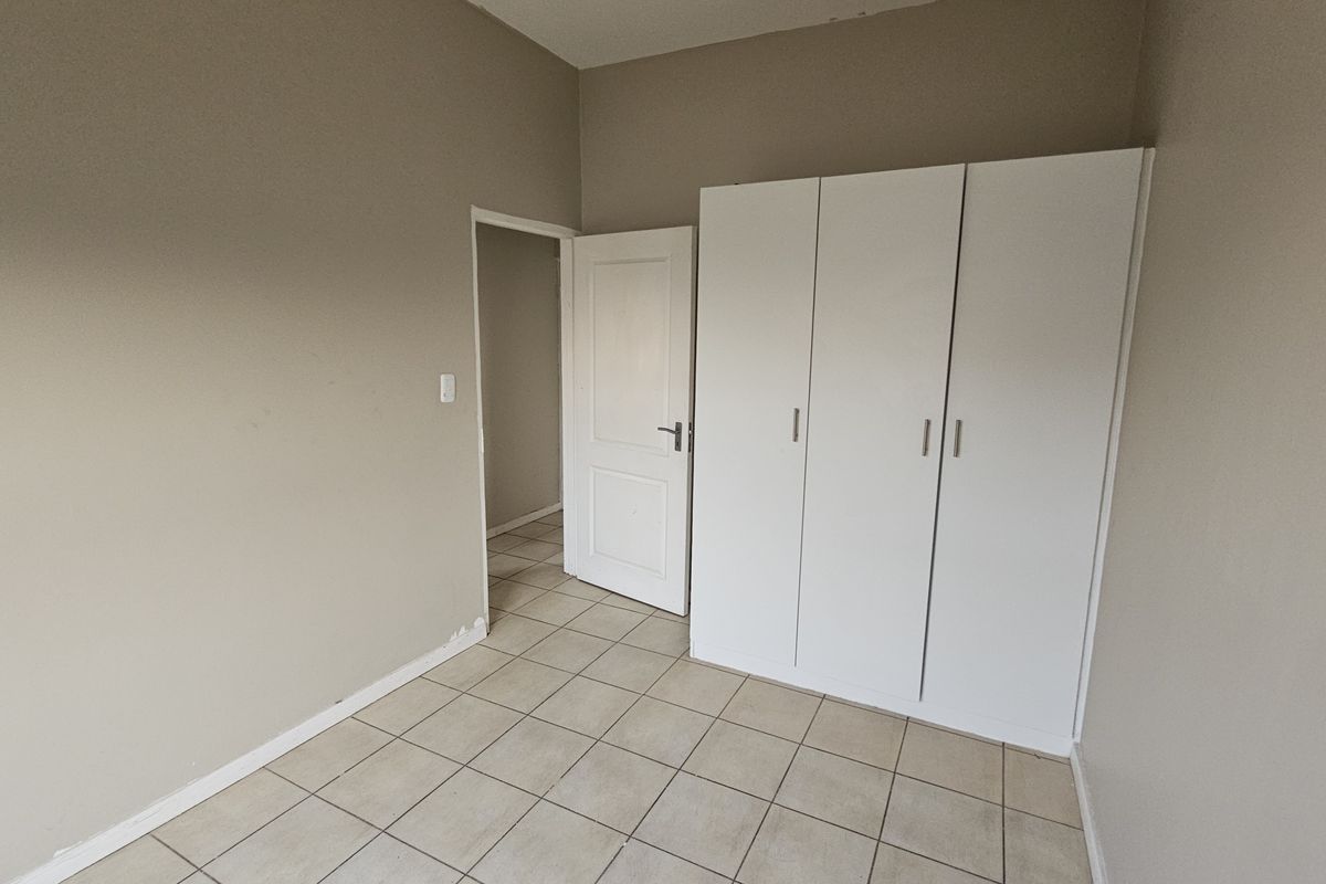 A vacant bedroom featuring neutral wall tones, tiled flooring, and a functional built-in wardrobe with white cabinetry.