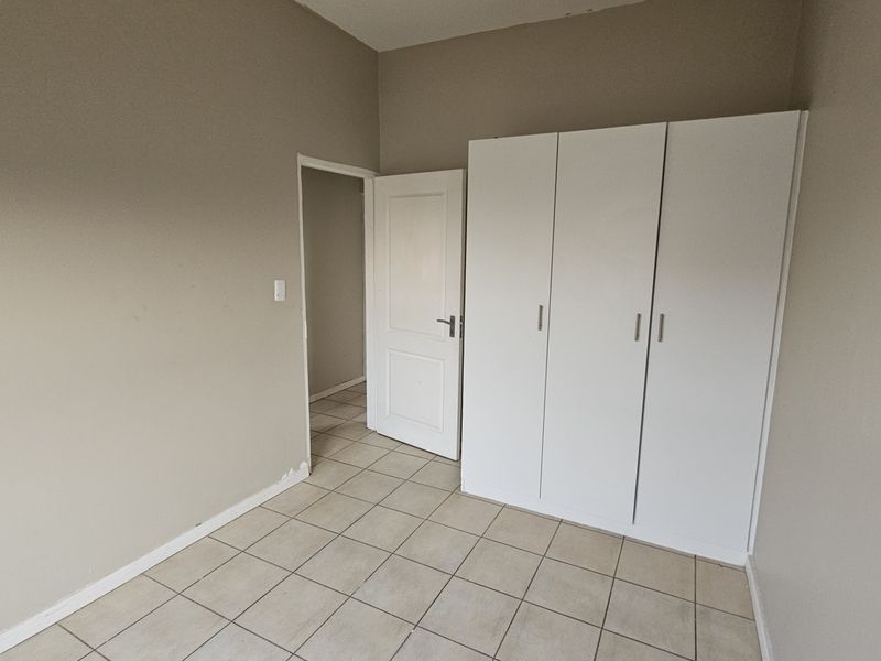 A vacant bedroom featuring neutral wall tones, tiled flooring, and a functional built-in wardrobe with white cabinetry.