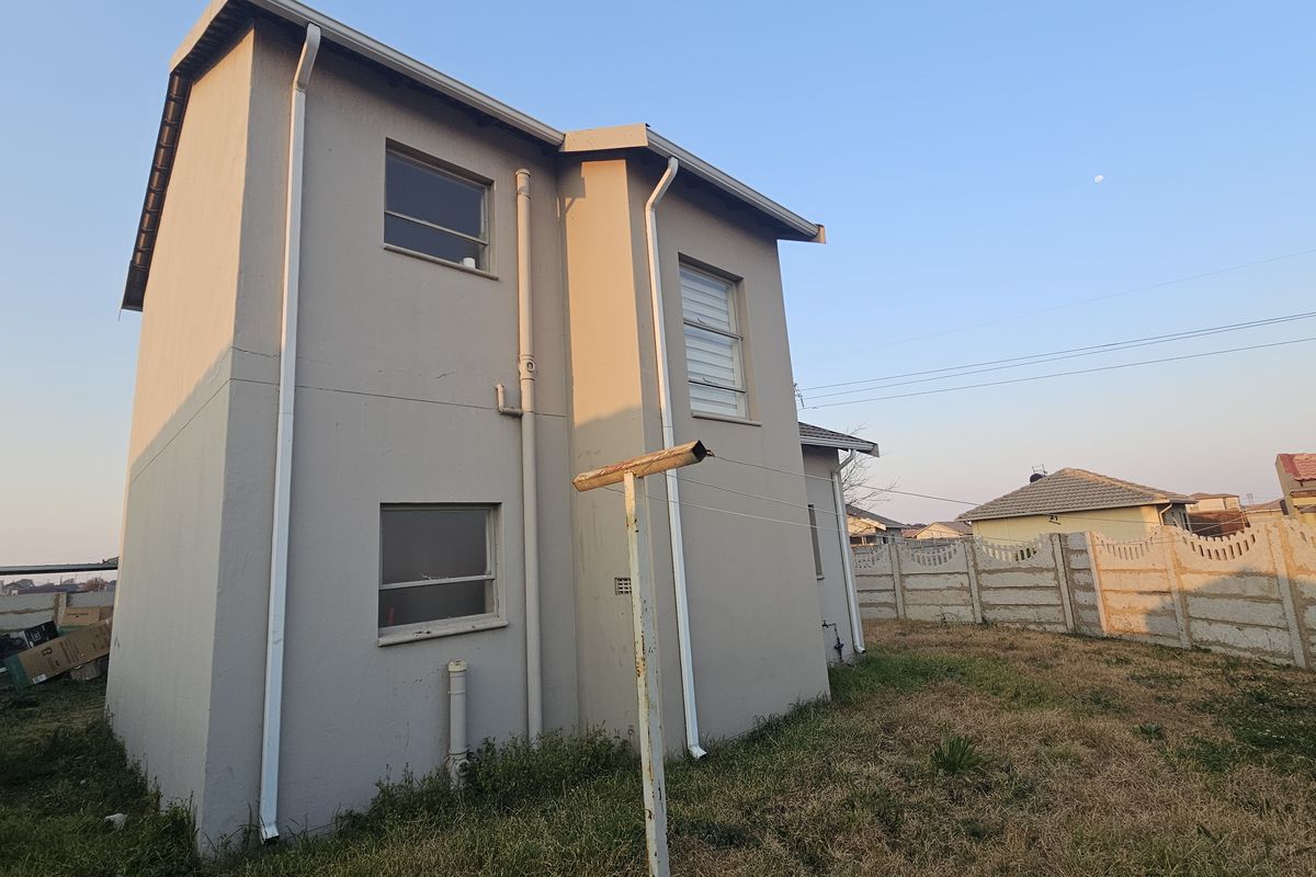 Rear view of a two-story residential property featuring exterior plaster walls, rainwater downpipes, and a precast concrete boundary wall.