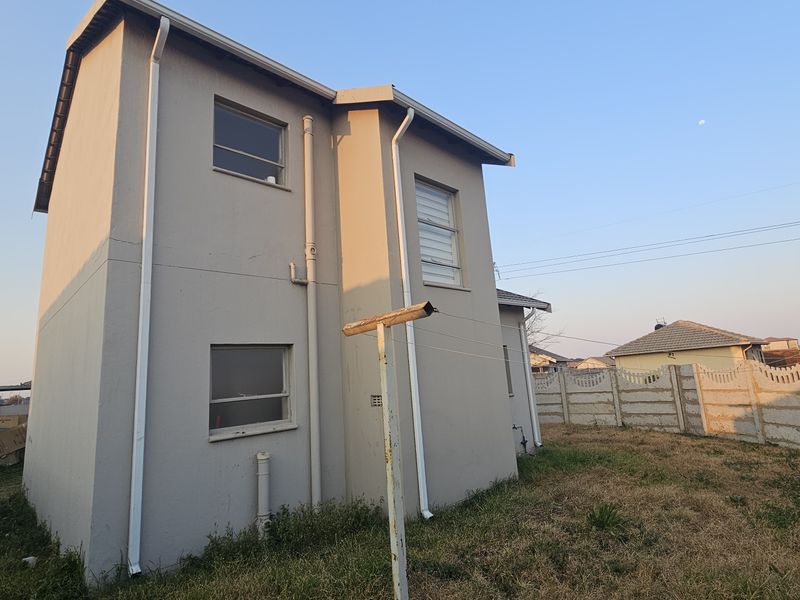Rear view of a two-story residential property featuring exterior plaster walls, rainwater downpipes, and a precast concrete boundary wall.