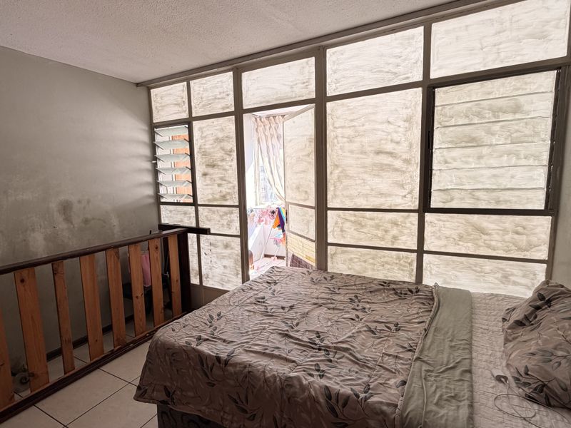 Bedroom featuring large glass window panels, tiled flooring, and a wooden balustrade, requiring cosmetic updates to wall finishes and window frames.