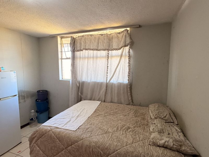 A bedroom featuring tiled flooring and security bars on the window, showing signs of wall staining and wear requiring maintenance.