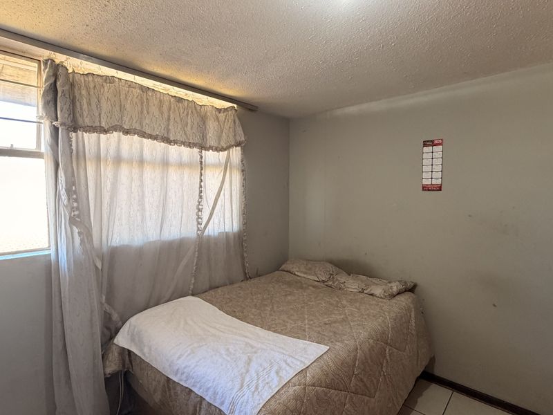 A bedroom featuring tiled flooring and a window with security bars, requiring cosmetic updates to the walls and ceiling to improve its overall condition.