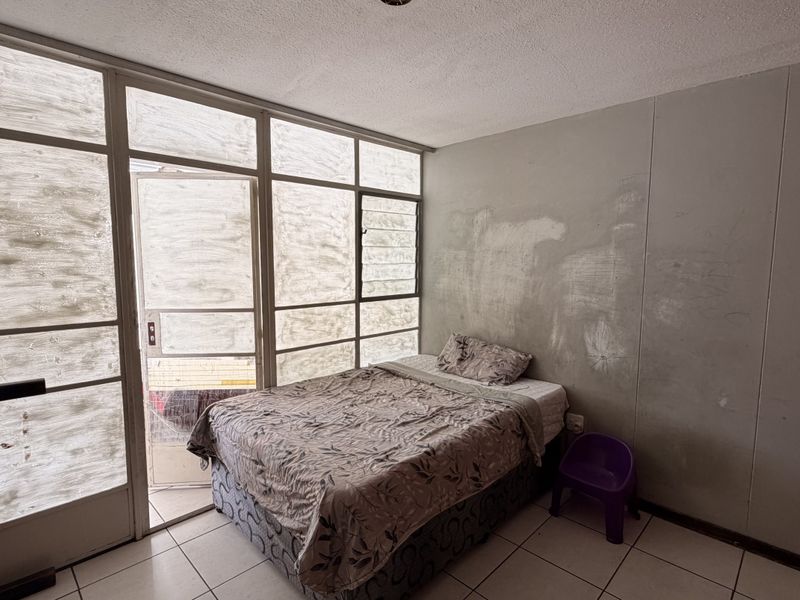 A bedroom featuring tiled flooring and a large glass panel wall with integrated louvre windows and access to an outdoor area.