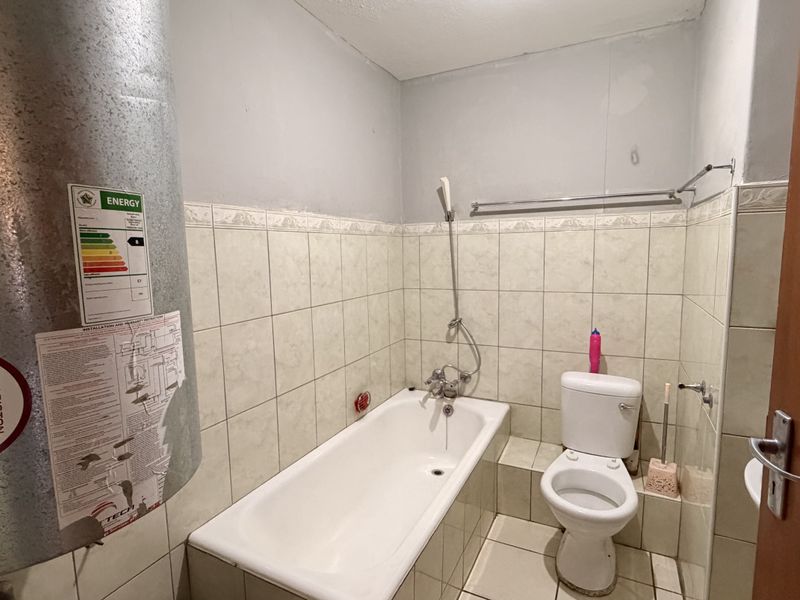 A functional bathroom featuring a bathtub, toilet, and an electric water heater, requiring cosmetic updates to the wall finishes and fixtures.
