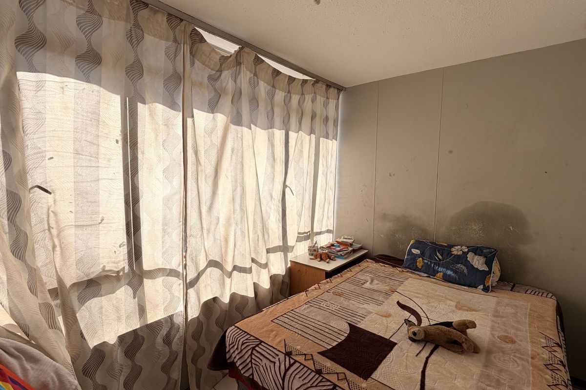 A bedroom featuring a large window with curtain track, showing visible water damage and staining on the wall surface requiring maintenance.