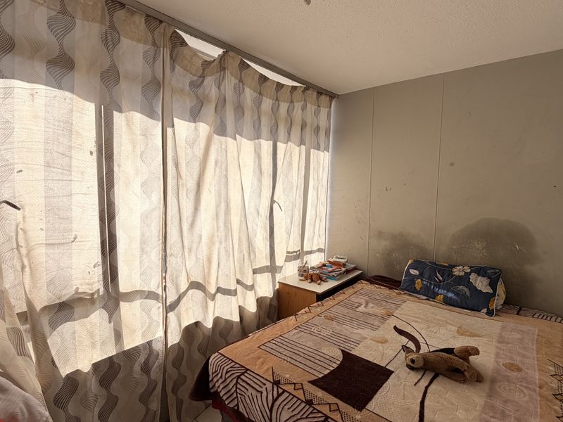 A bedroom featuring a large window with curtain track, showing visible water damage and staining on the wall surface requiring maintenance.