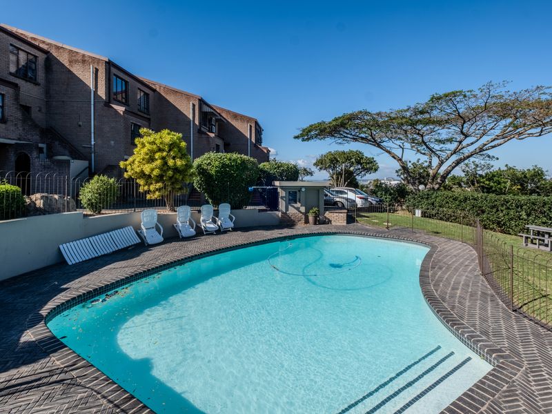 Outdoor swimming pool area featuring brick paving, perimeter fencing, and a landscaped garden setting within the townhouse complex.