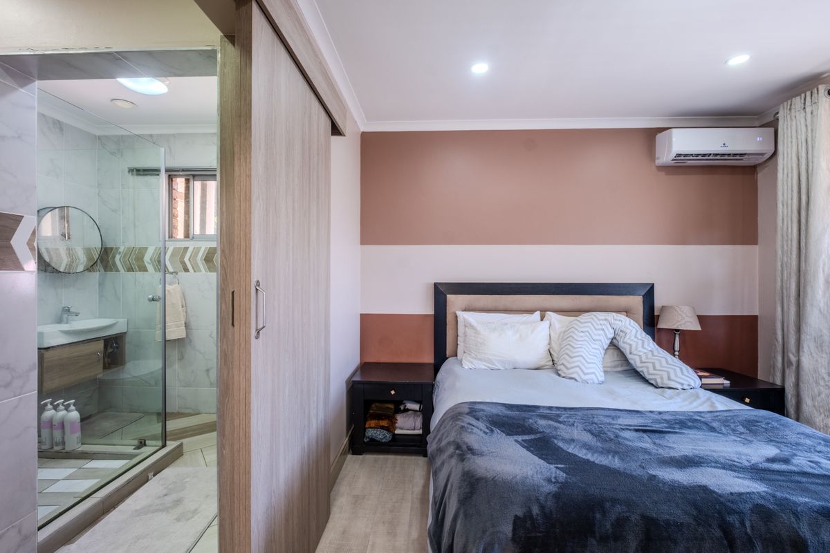 A well-maintained bedroom featuring an integrated en-suite bathroom with a glass shower, modern vanity, and a split-system air conditioning unit.