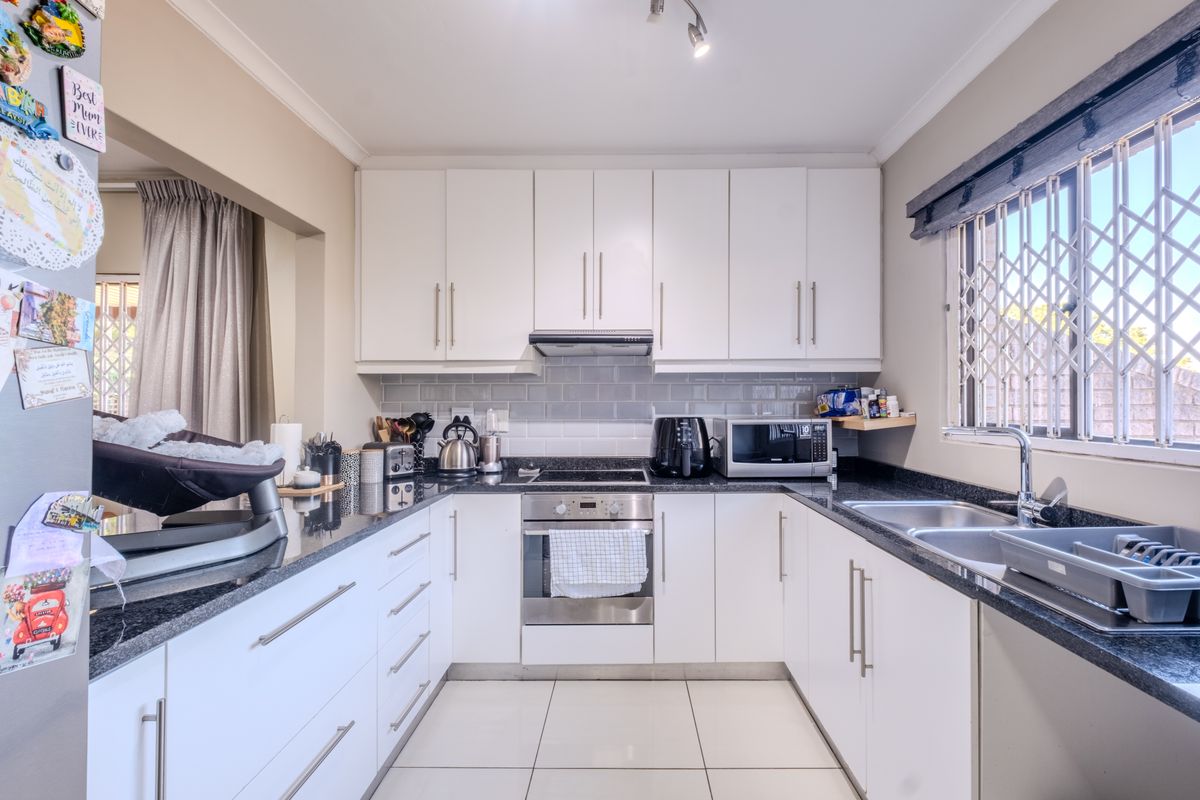 A well-maintained kitchen featuring white cabinetry, granite countertops, a built-in oven with hob, and a double sink with a window view.