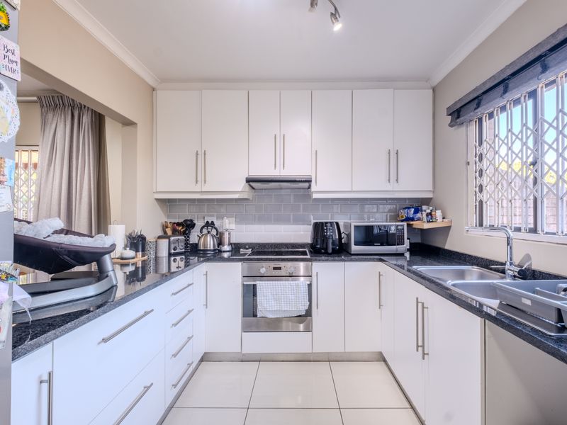 A well-maintained kitchen featuring white cabinetry, granite countertops, a built-in oven with hob, and a double sink with a window view.