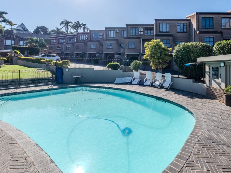 A communal swimming pool area featuring brick paving and a retaining wall, set against a backdrop of multi-level townhouse units.