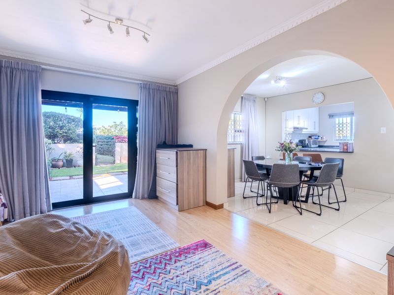 Open plan living and dining area featuring an arched transition, laminate and tiled flooring, and direct access to a paved patio through sliding glass doors.