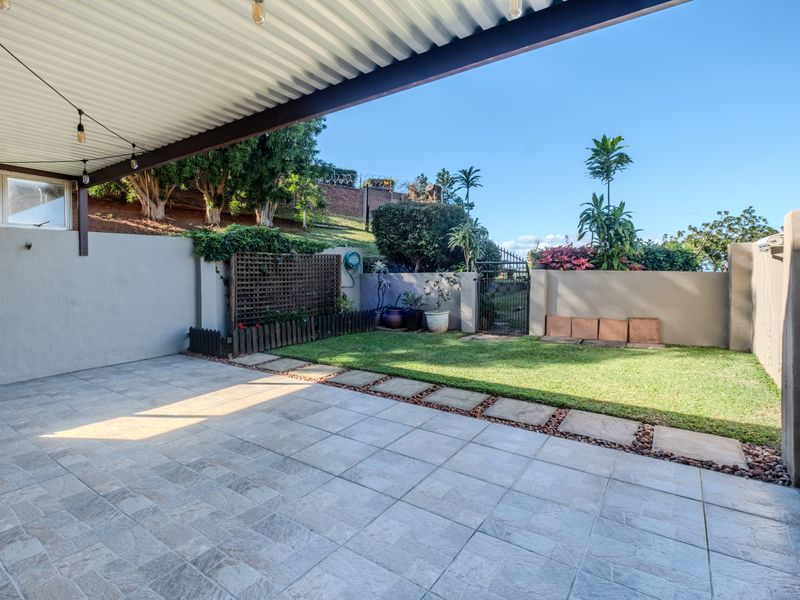 A covered patio area featuring tiled flooring, a corrugated metal roof, and direct access to a private garden with boundary walls and a gate.