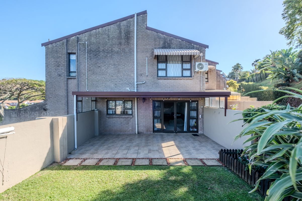Rear view of the townhouse featuring a tiled patio area, brick facade, and a small private garden space.