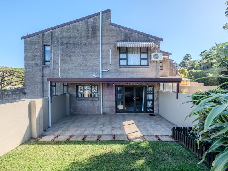 Rear view of the townhouse featuring a tiled patio area, brick facade, and a small private garden space.