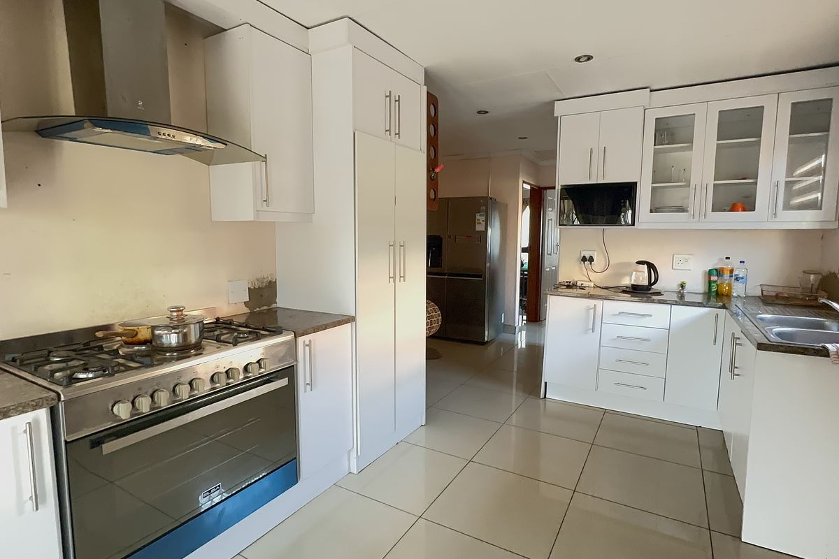 A functional kitchen featuring white cabinetry, a gas stove with extractor fan, double sink, and tiled flooring, with some unfinished wall finishes.