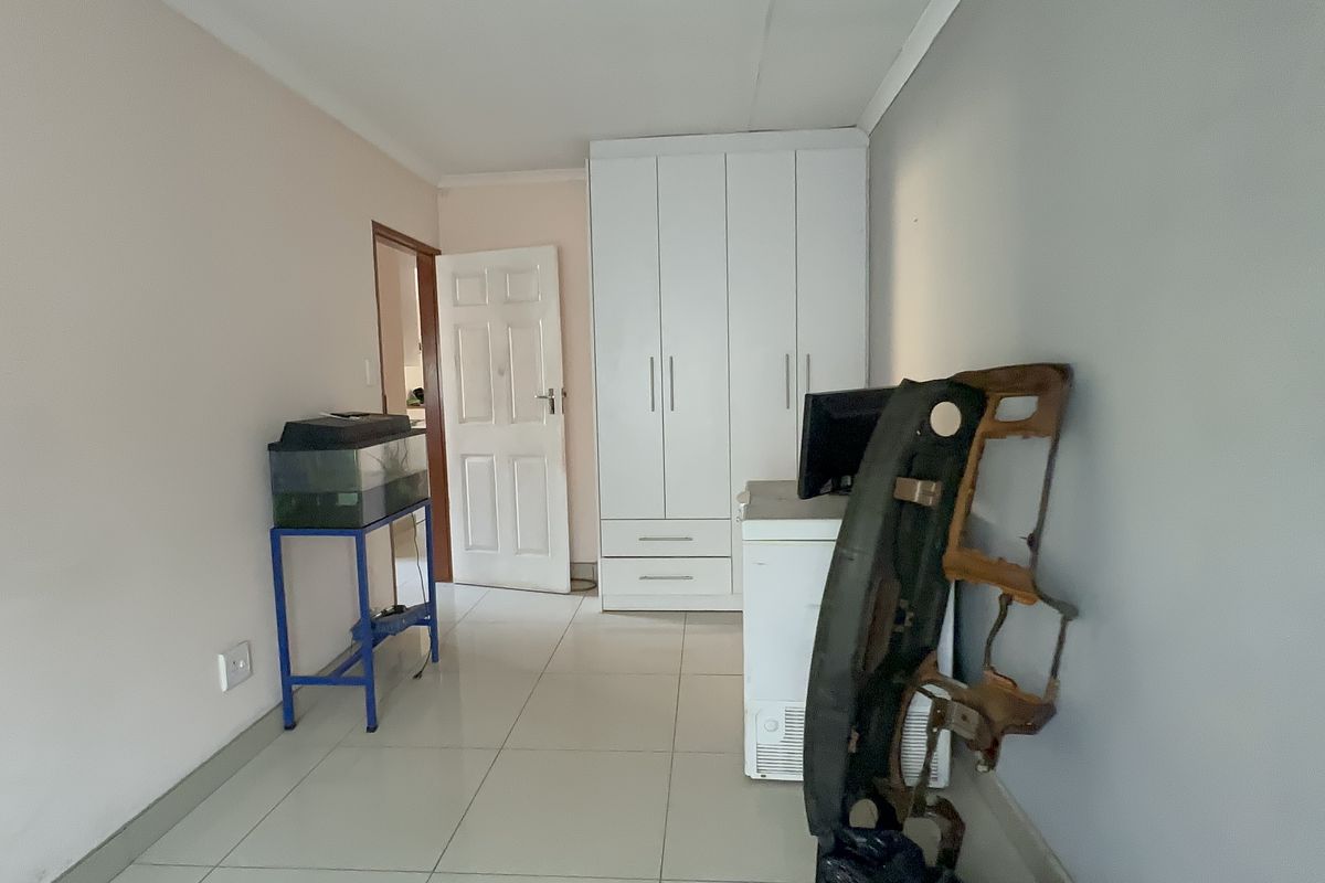 A bedroom featuring neutral walls, tiled flooring, and a white built-in wardrobe providing ample storage space.