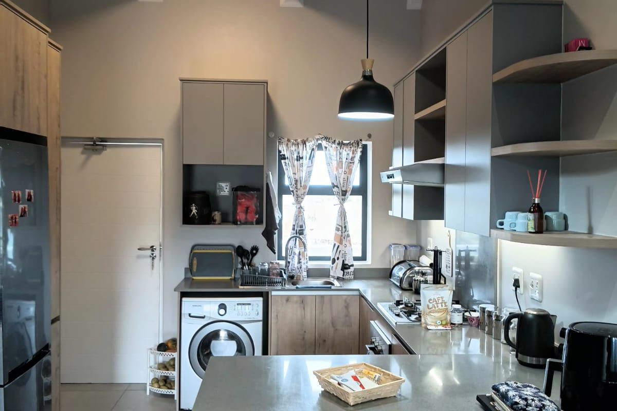 Modern kitchen featuring exposed timber ceiling beams, sleek cabinetry, stone countertops, and integrated laundry facilities in a well-lit, functional layout.