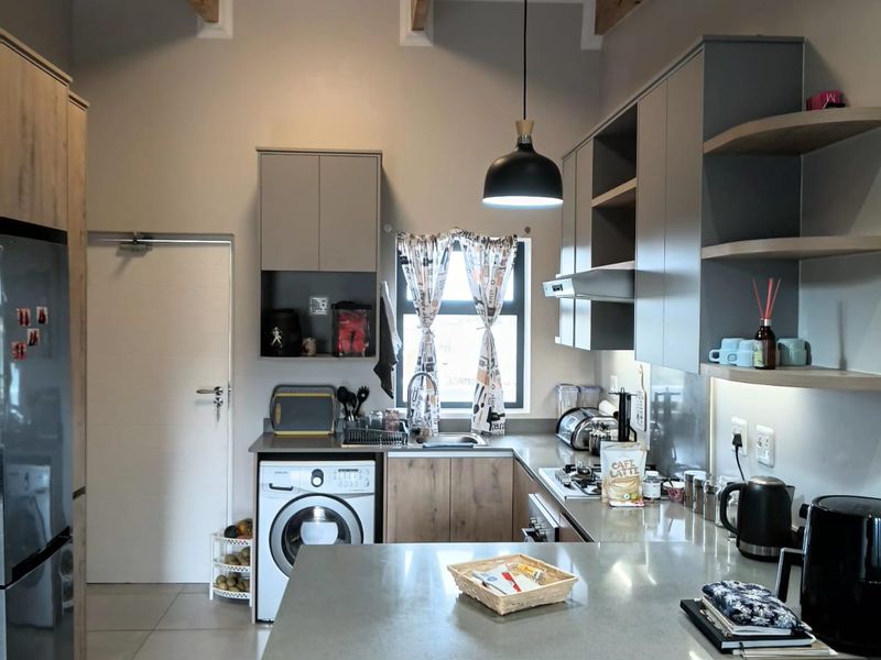 Modern kitchen featuring exposed timber ceiling beams, sleek cabinetry, stone countertops, and integrated laundry facilities in a well-lit, functional layout.