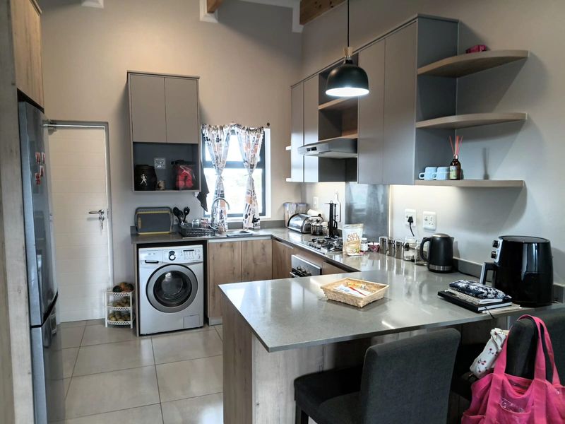 Modern kitchen featuring sleek grey and wood-tone cabinetry, stone countertops, integrated laundry appliances, and a functional breakfast bar layout.