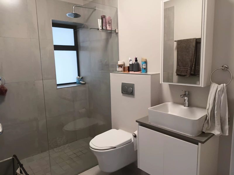 Modern bathroom featuring a wall-mounted toilet with concealed cistern, glass-enclosed rain shower, and a sleek vanity with a vessel sink.