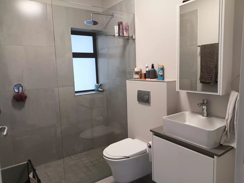 Modern bathroom featuring a walk-in shower with glass screen, wall-mounted toilet with concealed cistern, and a contemporary vessel sink vanity unit.