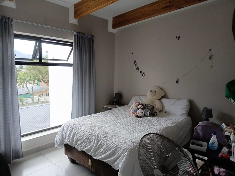 A bedroom featuring exposed timber ceiling beams, tiled flooring, and an aluminium window frame with views of the surrounding area.