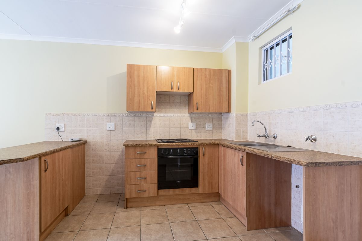 A functional kitchen featuring wood-look cabinetry, laminate countertops, built-in oven and hob, tiled backsplash, and tiled flooring with a security-barred window.
