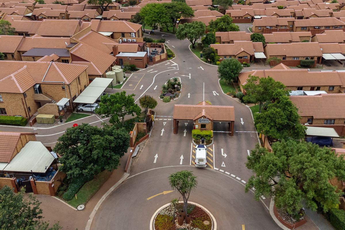 Aerial view of a residential complex featuring a secure gated entrance, paved internal roads, and uniform brick-built units with tiled roofs.