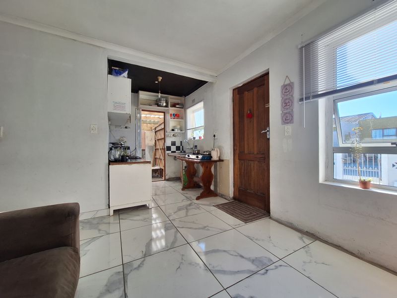 Open plan living area featuring tiled flooring, timber entrance door, and a compact kitchen nook with basic cabinetry and sink.