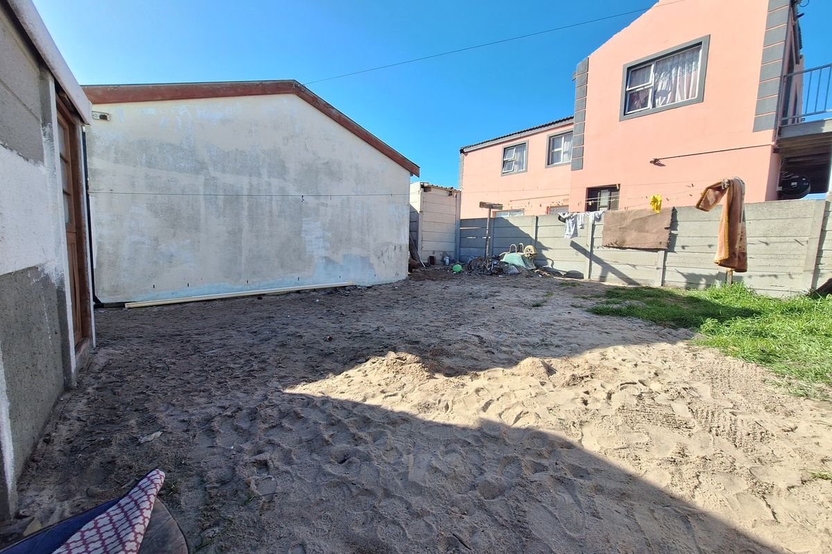 Rear yard area featuring a sandy ground surface, precast concrete boundary wall, and views of the adjacent residential building exterior.