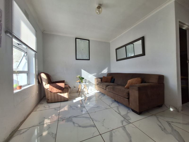 A living room featuring marble-look floor tiles, neutral walls, and natural light from a side window.