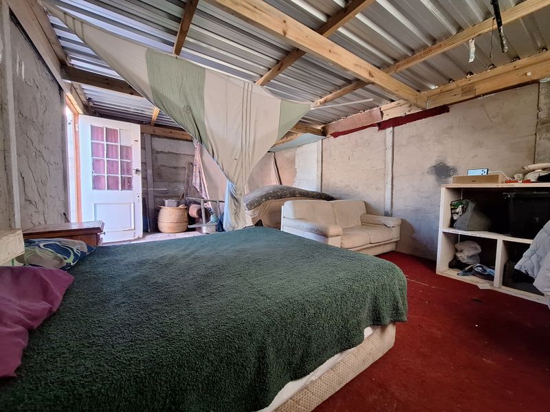 A rustic bedroom space featuring exposed concrete block walls and an open timber roof structure with corrugated metal sheeting.
