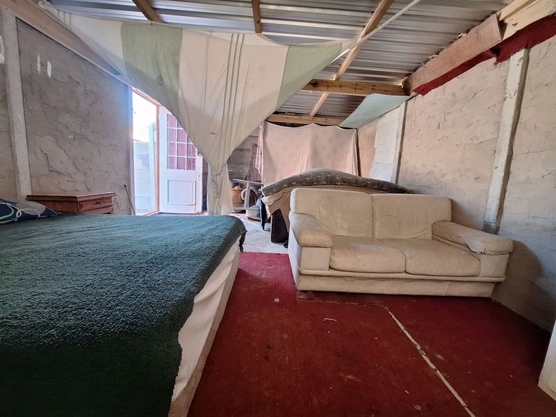 A rustic bedroom space featuring exposed timber roof beams, corrugated metal ceiling, and unfinished masonry walls with direct access to the exterior.