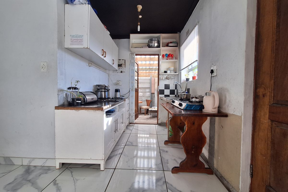 A compact kitchen featuring white cabinetry, marble-look floor tiles, and a black ceiling, offering potential for a modern renovation.