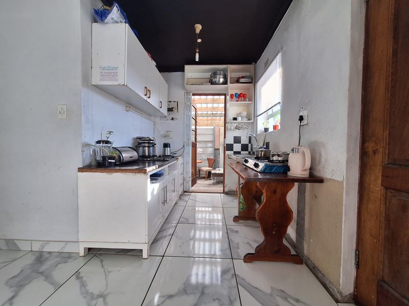 A compact kitchen featuring white cabinetry, marble-look floor tiles, and a black ceiling, offering potential for a modern renovation.