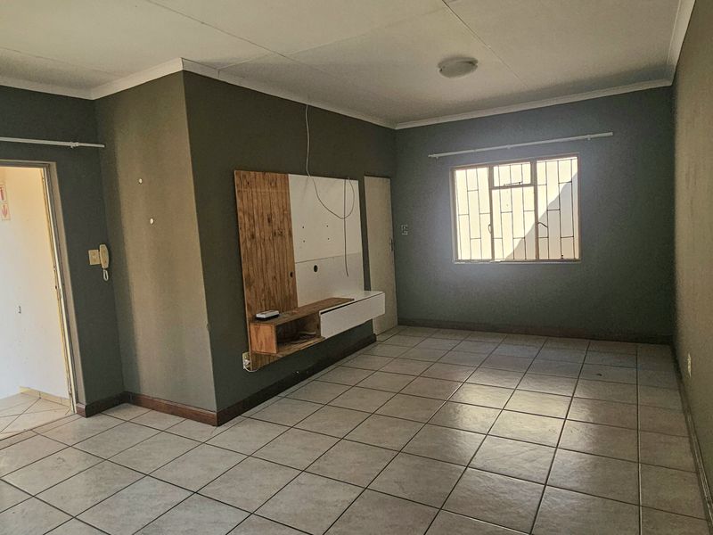 An empty living room featuring tiled flooring, a built-in media console, and a sliding glass door with security bars leading to the exterior.