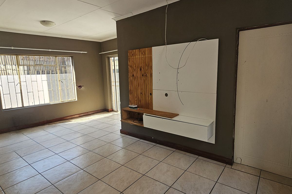 Spacious living area featuring tiled flooring, a built-in media console, and security bars on the windows, offering a blank canvas for renovation.