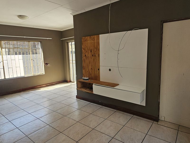 Spacious living area featuring tiled flooring, a built-in media console, and security bars on the windows, offering a blank canvas for renovation.