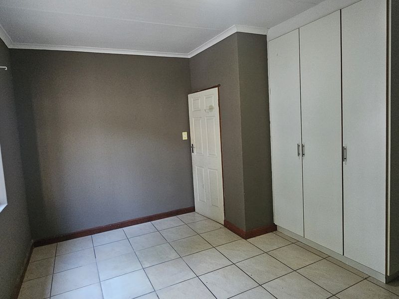 A clean, empty bedroom featuring neutral grey walls, tiled flooring, and built-in cupboards with security bars on the window.