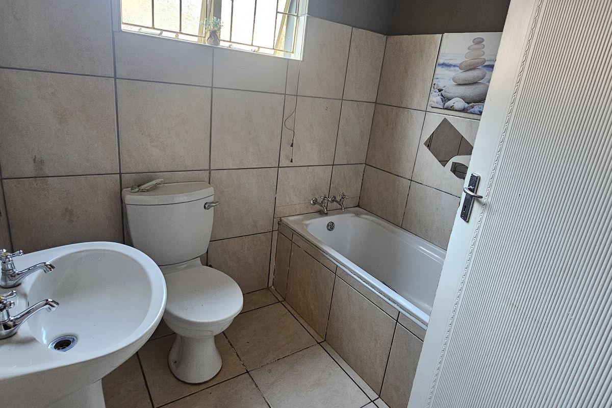 A functional bathroom featuring a pedestal basin, toilet, and a built-in bathtub with neutral wall and floor tiling.
